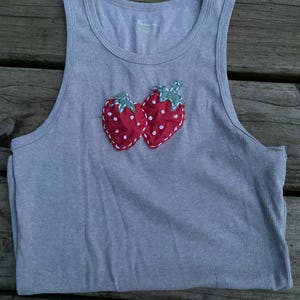 May include: A gray ribbed tank top with a red and white embroidered strawberry design.