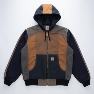 May include: A colour-blocked hooded jacket featuring panels of navy blue, brown, and grey. The jacket has a full-length front zip, a quilted black interior lining, ribbed cuffs, and a Carhartt brand patch on the chest pocket.