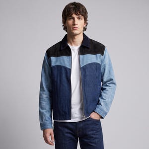 Op de afbeelding: Een jack met ritssluiting, voorzien van een zwarte kraag en schouderpas, een lichtblauw middengedeelte en een donkerblauw onderstuk en mouwen. Het jack wordt gedragen over een effen wit T-shirt en een donkerblauwe spijkerbroek.