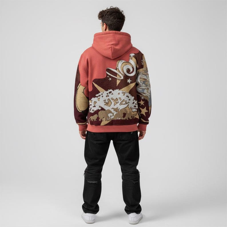 May include: A coral-colored hoodie with a detailed tapestry design on the back. The tapestry features a central tree motif, stars, and other decorative elements in shades of brown, beige, and white. The hoodie has a drawstring hood and ribbed cuffs.