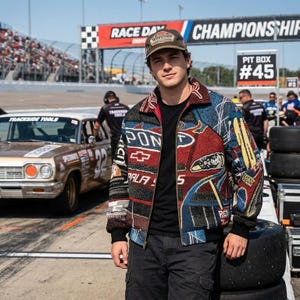 Peut inclure: Veste multicolore sur le thème de la course automobile avec fermeture éclair. La veste présente des motifs rouges, bleus et noirs, avec le mot "PALA" et un logo Chevrolet visibles. La personne porte une casquette marron avec du texte et un pantalon cargo noir.