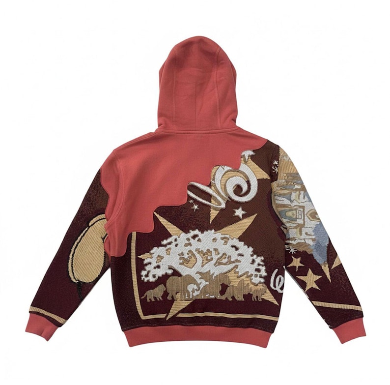 May include: A rust-colored hoodie with a detailed tapestry design on the back. The design includes a tree, elephants, stars, and swirling shapes in shades of brown, beige, and white. The hoodie has a hood and ribbed cuffs.