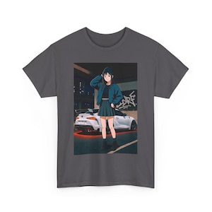 Puede incluir: Camiseta gris oscuro con una ilustración de estilo anime. El gráfico representa a una persona frente a un coche deportivo blanco con un resplandor rojo. La persona lleva una chaqueta azul, una falda y botas negras. Se ve graffiti en el fondo.