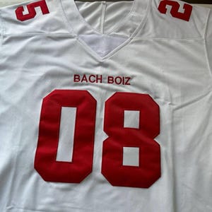 May include: White football jersey with red numbers and lettering. The jersey features the number "08" on the front and "5" and "2" on the shoulders. The text "BACH BOIZ" is embroidered in red above the number.
