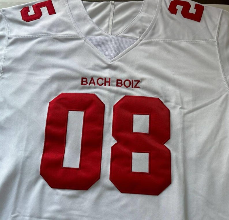 May include: White football jersey with red numbers and lettering. The jersey features the number "08" on the front and "5" and "2" on the shoulders. The text "BACH BOIZ" is embroidered in red above the number.