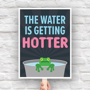 May include: A poster with the text "THE WATER IS GETTING HOTTER" in blue and pink. A cartoon frog with green skin and yellow eyes is in a gray bucket of water. The poster is held by a wooden stick.