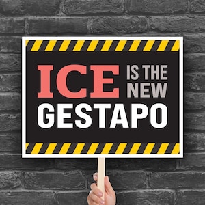 May include: A rectangular sign with the text "ICE IS THE NEW GESTAPO" in white, coral, and gray letters. The sign has a black background with yellow and black diagonal stripes at the top and bottom. The sign is held by a wooden stick.