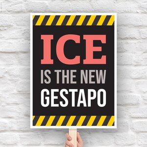 May include: A rectangular sign with the text "ICE IS THE NEW GESTAPO" in coral, white, and gray lettering. The sign has black and yellow diagonal stripes at the top and bottom, held by a wooden stick.