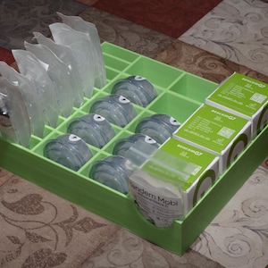 May include: A green plastic storage box with multiple compartments. The box contains clear plastic containers, some with a green lid, and several small boxes with white labels. The labels have the text "Medtronic MiniMed 640G" on them.