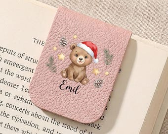 May include: A pink rectangular magnetic bookmark with a textured surface featuring a brown bear wearing a red Santa hat, surrounded by small stars and pinecones. The name Emil is printed in black script below the bear illustration.