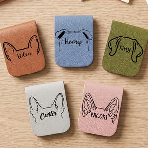 May include: Five rectangular magnetic bookmarks in tan, blue, olive green, light grey, and pink. Each features a black line drawing of animal ears and a name printed in script: Aiden, Henry, Kitty, Carter, and Nicola. The bookmarks have a textured finish.