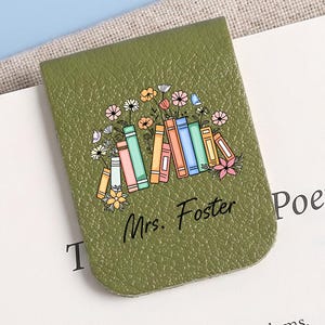 May include: A green leather bookmark with a floral and book design. The bookmark has the text "Mrs. Foster" in cursive. The bookmark is on a book with the word "Poetry" visible.