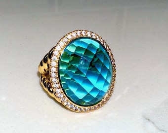 May include: A gold ring with a large oval blue gemstone surrounded by a halo of small clear stones.
