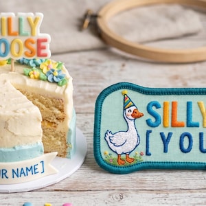 Op de afbeelding: Een grillige taart met een ganzenfiguur en de tekst "Silly Goose". Daarnaast een patch met een ganzenillustratie en de tekst "Silly Goose [Your Name]" in kleurrijke letters.
