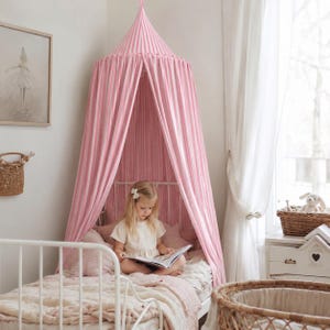 May include: A conical bed canopy featuring vertical pink and white stripes, suspended from the ceiling to drape over a white metal bed frame. The fabric creates a tent-like enclosure around the bed, providing a soft, draped aesthetic.