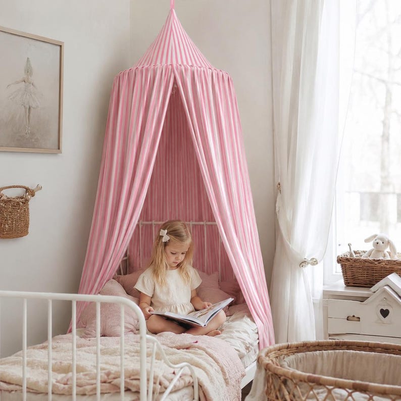May include: A conical bed canopy featuring vertical pink and white stripes, suspended from the ceiling to drape over a white metal bed frame. The fabric creates a tent-like enclosure around the bed, providing a soft, draped aesthetic.