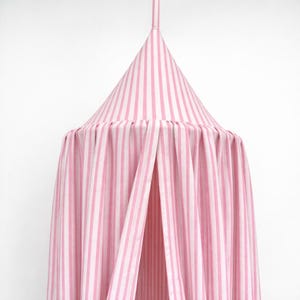 May include: A conical fabric canopy featuring vertical light pink and white stripes. The structure includes a pointed top section that transitions into a pleated, flowing curtain design that hangs downward, creating a soft and draped appearance.