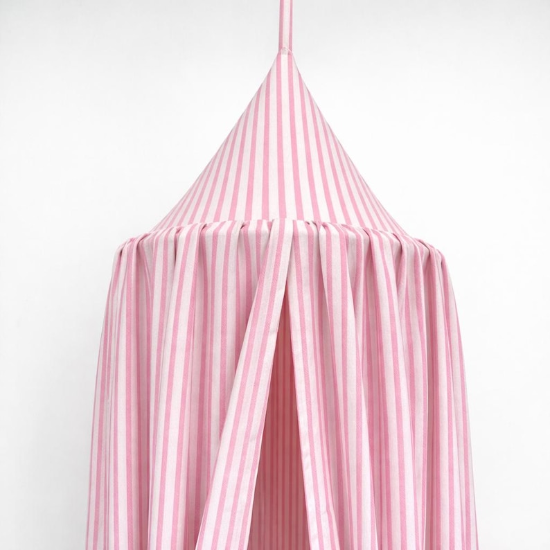 May include: A conical fabric canopy featuring vertical light pink and white stripes. The structure includes a pointed top section that transitions into a pleated, flowing curtain design that hangs downward, creating a soft and draped appearance.