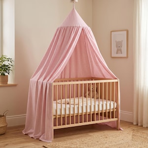 May include: A light pink and white gingham patterned fabric canopy suspended over a light-colored wooden crib. The crib features vertical slats, a white mattress, and a small plush bear toy resting inside the frame on the mattress surface.