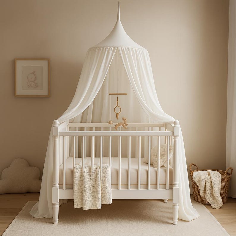 May include: A white wooden crib with a canopy and a cream-colored blanket. A mobile with wooden shapes hangs above the crib. A framed picture and a wicker basket are also in the room. The crib is approximately 52 inches long.