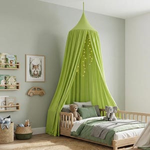 May include: A lime green fabric bed canopy hangs from the ceiling over a wooden toddler bed. The canopy features draped fabric panels and a string of warm white fairy lights hanging inside. The bed includes a white mattress, green bedding, and pillows.
