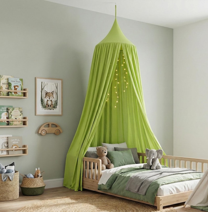 May include: A lime green fabric bed canopy hangs from the ceiling over a wooden toddler bed. The canopy features draped fabric panels and a string of warm white fairy lights hanging inside. The bed includes a white mattress, green bedding, and pillows.