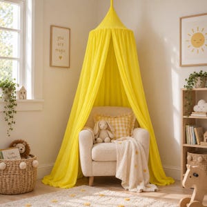 May include: A bright yellow fabric canopy suspended from the ceiling, draped over a cream-colored upholstered armchair. The chair features a yellow and white gingham throw pillow, a plush rabbit toy, and a cream-colored blanket with yellow pom-poms.