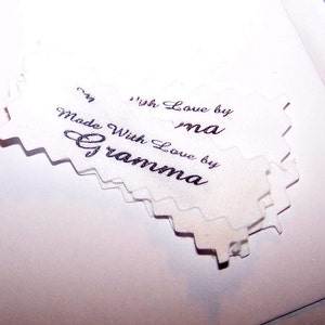 Puede incluir: Una pila de etiquetas de tela blanca con bordes festoneados. Las etiquetas est&aacute;n impresas con el texto "Made with Love by Gramma" y "With Love by ma".