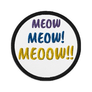 May include: A round white patch with a black border. The patch has the words "MEOW MEOW! MEOOW!!" embroidered in purple, blue, and yellow.