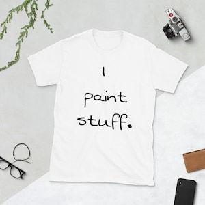 May include: A white short-sleeved t-shirt featuring the black text "I paint stuff." printed in a simple, handwritten-style font across the centre of the chest. The garment has a crew neckline and a standard fit, presented on a neutral surface.