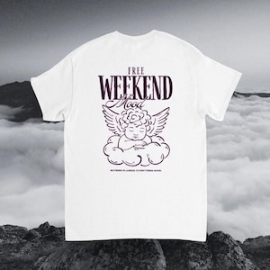 Könnte beinhalten: Ein weißes Kurzarm-T-Shirt mit einer dunkelvioletten Grafik auf der Rückseite. Das Design zeigt den Text "FREE WEEKEND Mood" über einer Strichzeichnung eines auf einer Wolke schlafenden Cherubs und darunter den Text "NOTHING PLANNED. EVERYTHING GOOD.".