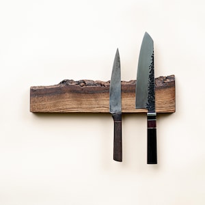 May include: A wooden knife holder with two knives. The holder is made of dark brown wood with a natural edge. One knife has a dark wooden handle and a long, thin blade. The other knife has a black handle and a wide blade.