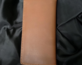 May include: A rectangular, tan leather wallet with a smooth surface. The wallet is stitched with a lighter brown thread around the edges. The wallet is closed and appears to be empty.