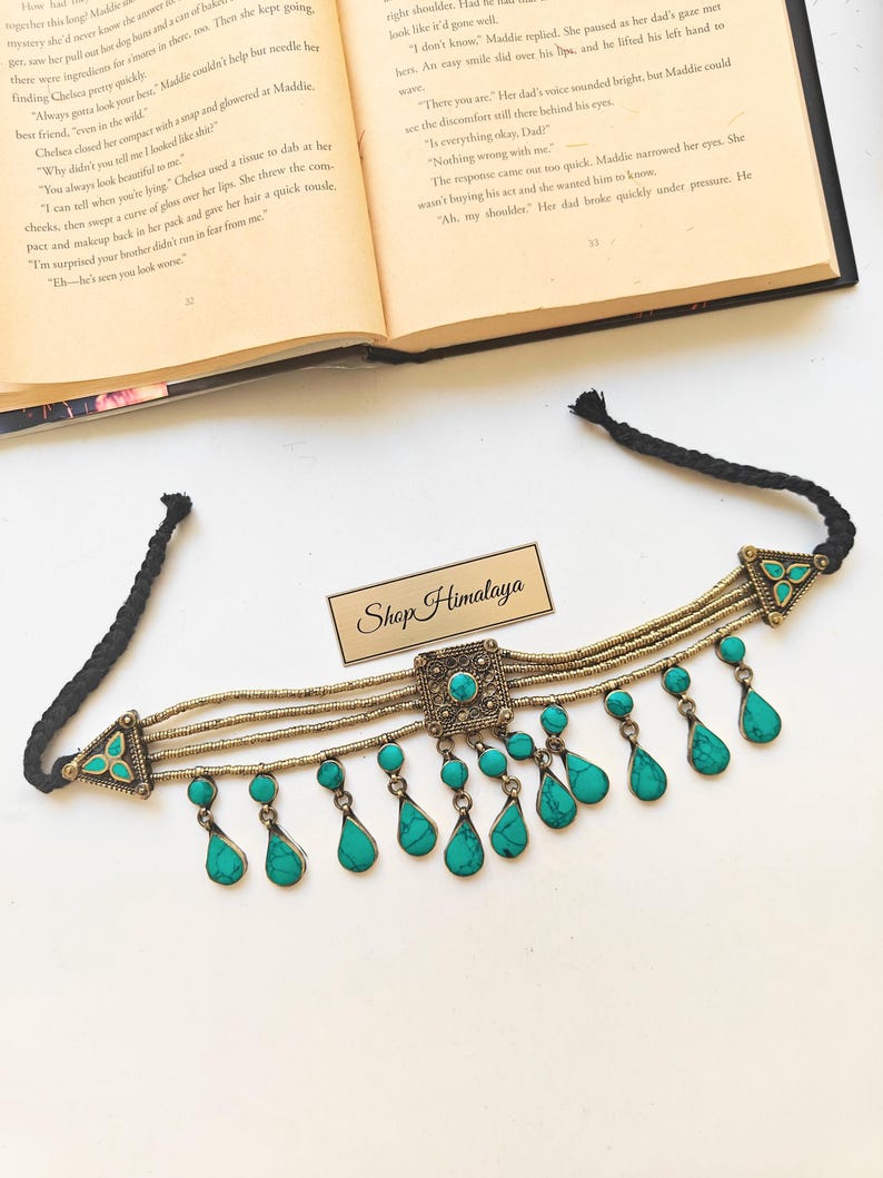 May include: A handcrafted choker necklace with turquoise teardrop pendants and a central square pendant. The necklace features a black cord and gold-toned metal accents, with the text "Shop Himalaya" on a small tag.