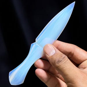 Puede incluir: Una daga de ópalo azul y blanco con una punta puntiaguda y un mango redondeado.