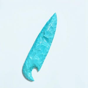 May include: A light blue, arrowhead-shaped, stone knife with a textured surface.