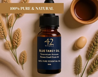 May include: A dark amber glass bottle of Blue Tansy Oil with a black dropper top. The label reads "42 RITUALS BLUE TANSY OIL" and "100% PURE ESSENTIAL OIL". The image includes dried plants, a small wooden bowl, and an egg-shaped object.