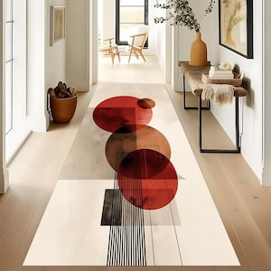 Può includere: Un tappeto rettangolare con un design astratto. Presenta grandi cerchi rossi e marroni, forme geometriche e strisce verticali bianche e nere su uno sfondo color crema. Il tappeto è posto in un corridoio.