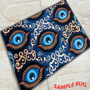 May include: A rectangular rug with a repeating pattern of large blue eyes on a dark blue background. The eyes have gold and brown accents, and the rug has a gray border. The text "SAMPLE RUG" is printed in red.
