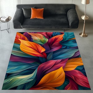 May include: A rectangular area rug featuring a vibrant, abstract design of large, overlapping leaves. The leaves display a gradient of colors, including orange, red, purple, teal, and green. The rug is placed on a gray floor, with a black sofa and orange pillow in the background.