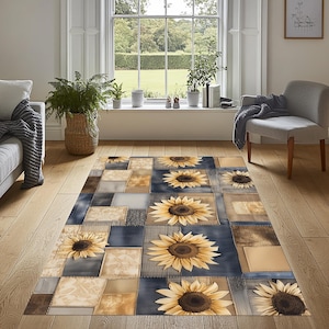May include: A rectangular area rug with a patchwork design featuring large sunflowers. The rug has a mix of blue, tan, and gray squares, with the sunflowers in the center of some squares. The rug is placed on a hardwood floor.