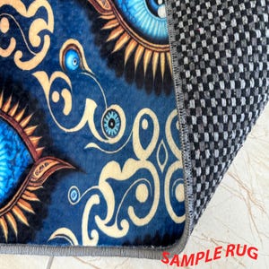 May include: A section of a blue rug with an eye design and gold swirls. The rug's edge is visible, showing a gray border and a checkered backing. The text "SAMPLE RUG" is in the bottom right corner.