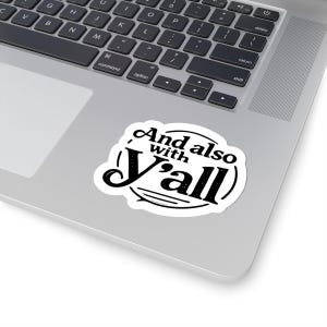 以下が含まれることがあります： 「And also with Y'all」のテキストが黒色のスタイリッシュなフォントで書かれた白いステッカー。ステッカーは銀色のノートパソコンに貼られており、背景にはキーボードが見えます。