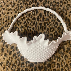 May include: A white milk glass basket with a ruffled edge and a handle. The basket is covered in small white dots.