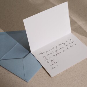 May include: A white card with a handwritten thank you note. The note says "Thank you so much for celebrating our big day with us! Your presence meant so much and we're so grateful you could share in the joy. With love, Anne."