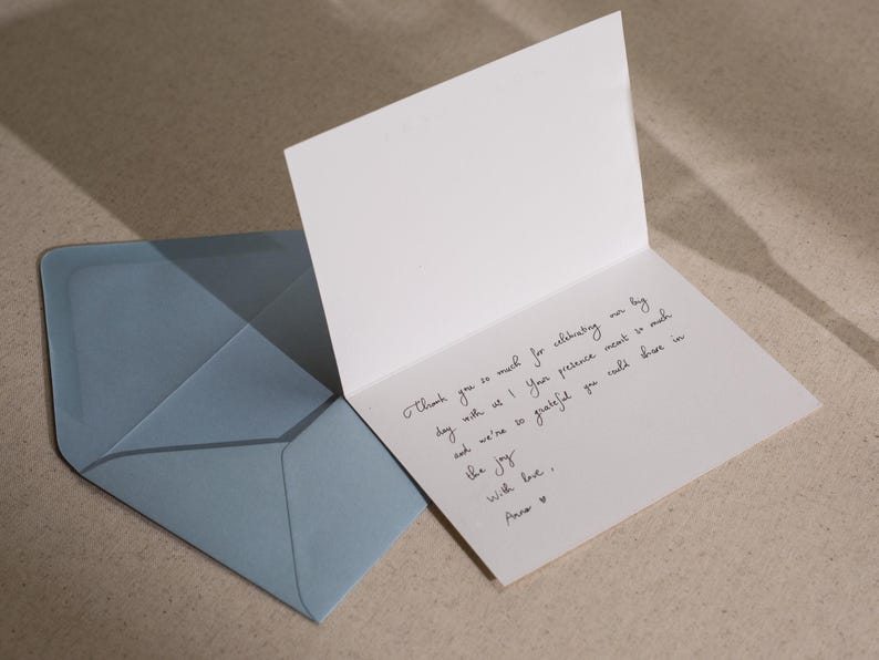May include: A white card with a handwritten thank you note. The note says "Thank you so much for celebrating our big day with us! Your presence meant so much and we're so grateful you could share in the joy. With love, Anne."