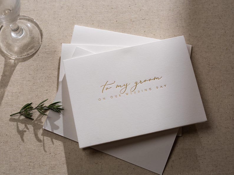 May include: White card with gold lettering that reads "To my groom on our wedding day".