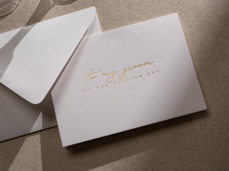 May include: A white card with gold foil lettering that reads "To my groom on our wedding day".