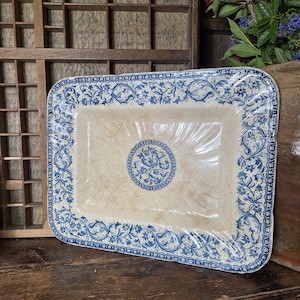 Può includere: Piatto da portata rettangolare in ceramica color crema con bordo floreale blu e medaglione centrale. Il piatto è avvolto in plastica trasparente. Il motivo floreale è un motivo classico ed elegante.