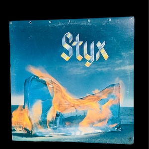 May include: Album cover for the band Styx, titled "Equinox". The artwork features a blue background with a block of ice containing flames. The band's name is in a stylized font.